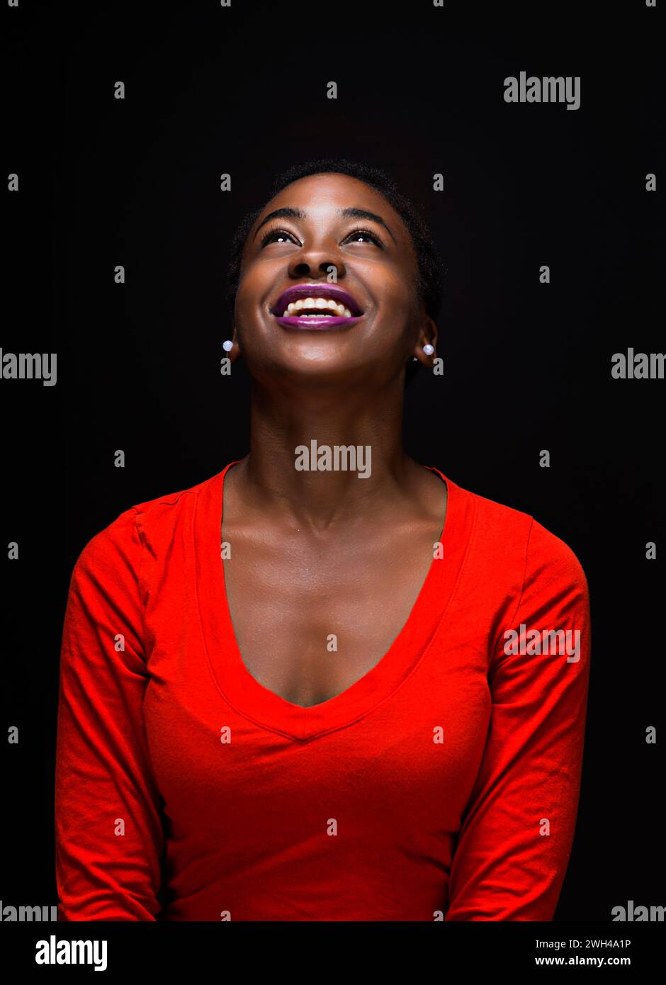 Strahlende junge Frau lächelt in rotem Oberteil vor schwarzem Hintergrund Stockfoto