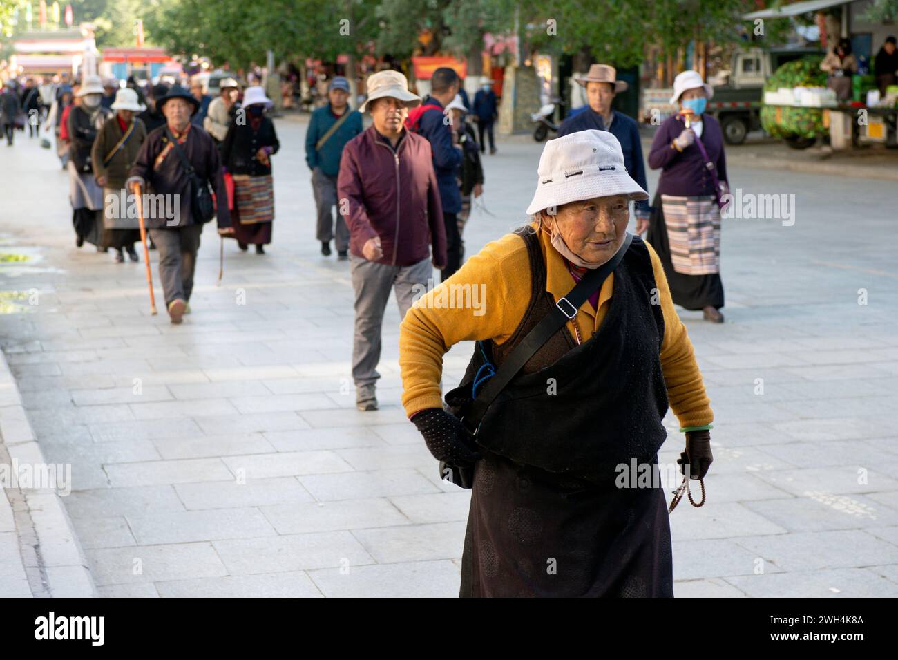 Eine ältere tibetische Frau trägt Gebetsperlen in ihrer Hand, während sie auf einem Bürgersteig von Lhasa City spaziert. Stockfoto