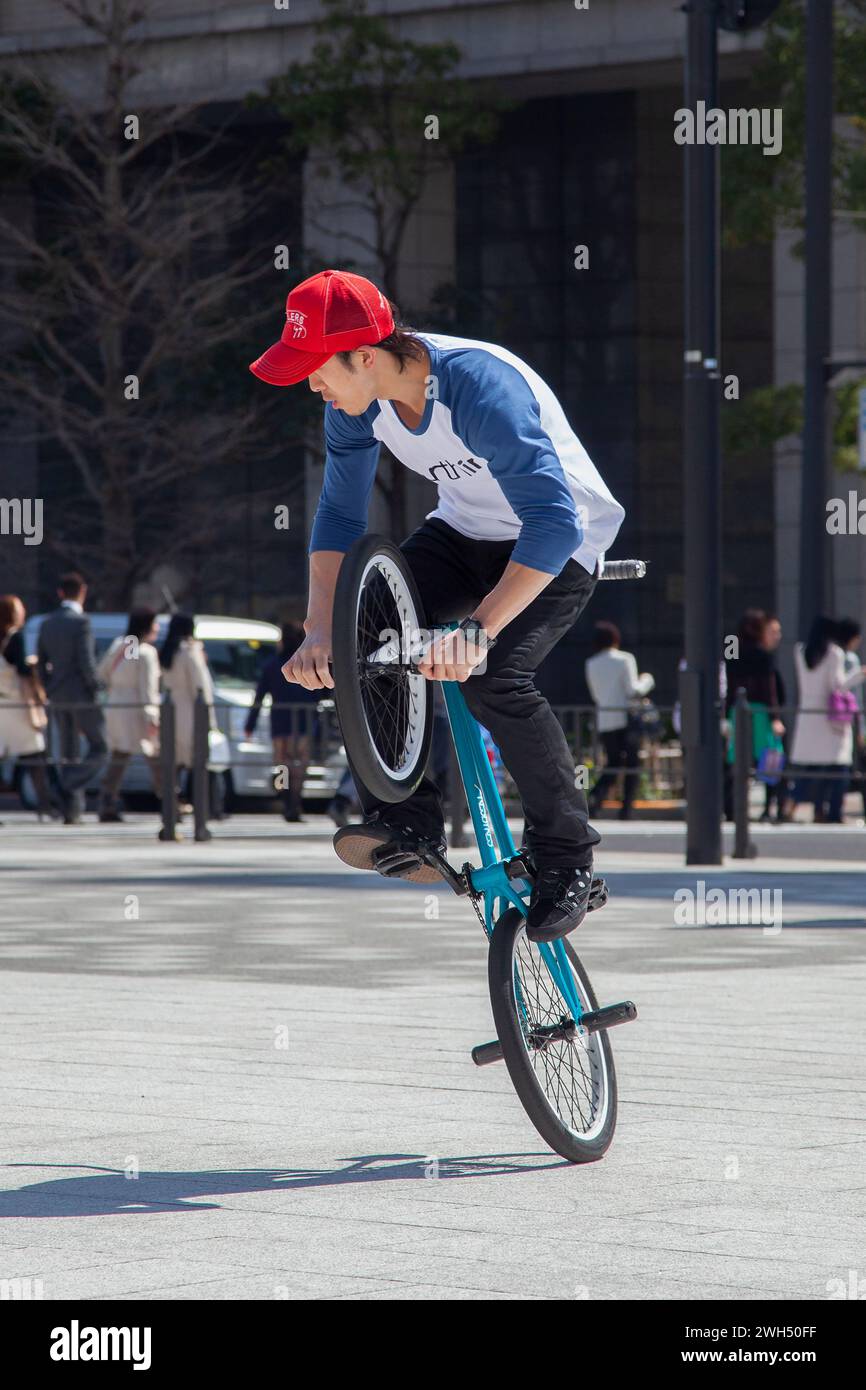 Ein japanischer BMX-Fahrer führt auf einem öffentlichen Platz mitten im Geschäftsviertel in Tokio, Japan, Tricks aus. Stockfoto