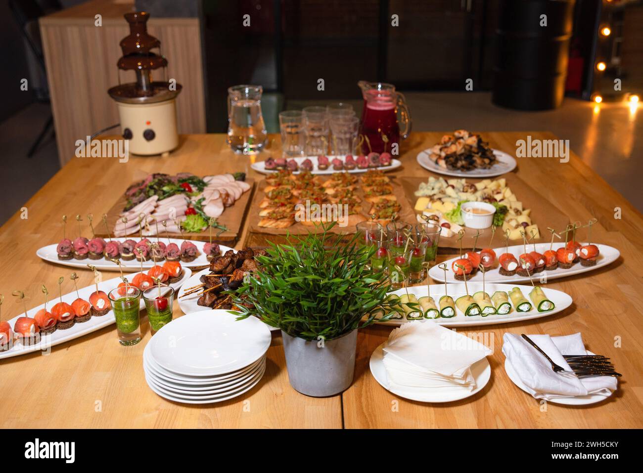 Ein elegant gestalteter Buffettisch mit einer Auswahl an Gourmetgerichten, darunter Canapés, Spieße und Schokoladenbrunnen für eine Veranstaltung. Stockfoto