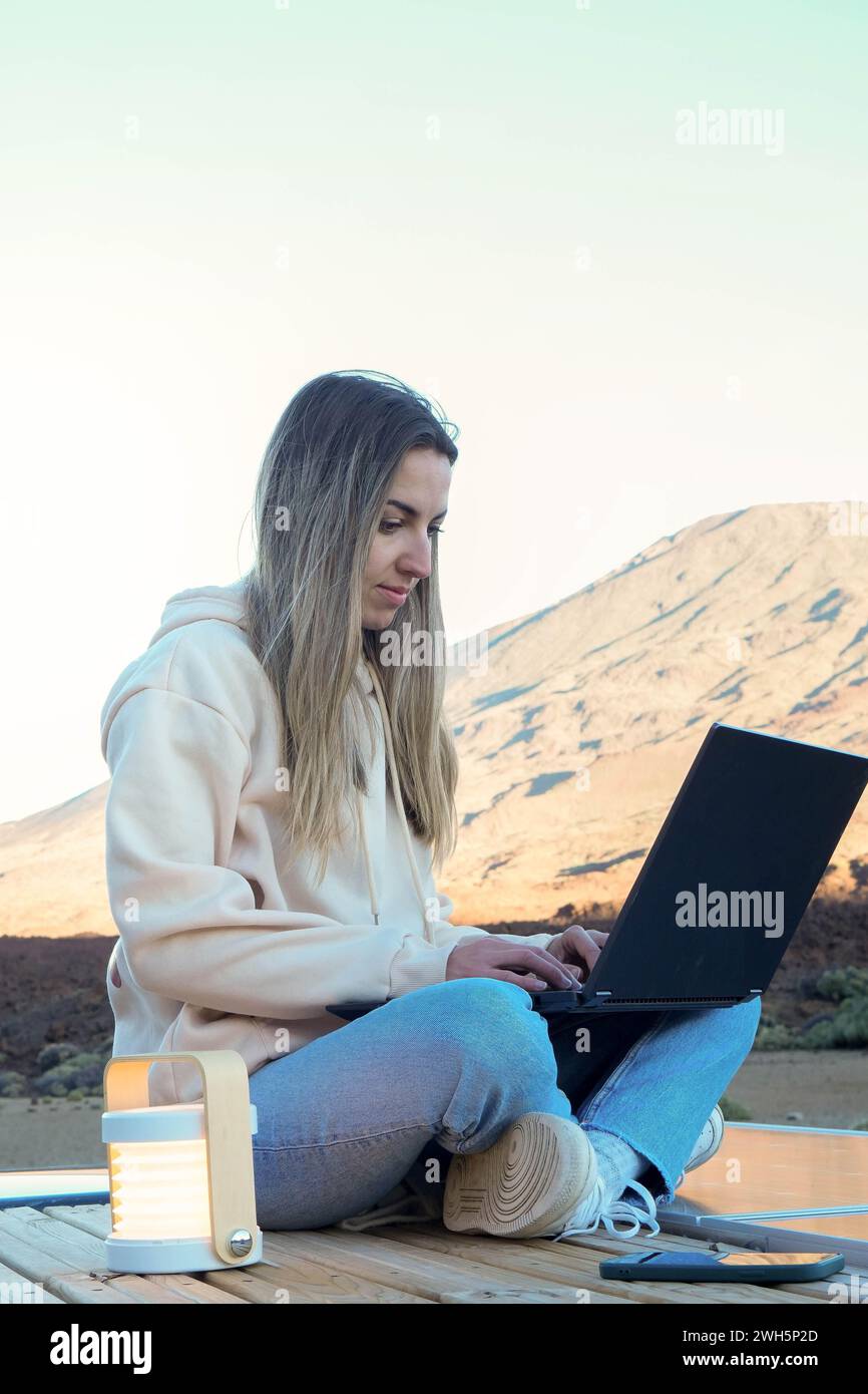 Eine junge Frau saß draußen auf dem Boden und arbeitete an ihrem Laptop mit dem wunderschönen Teide-Berg im Hintergrund. Stockfoto