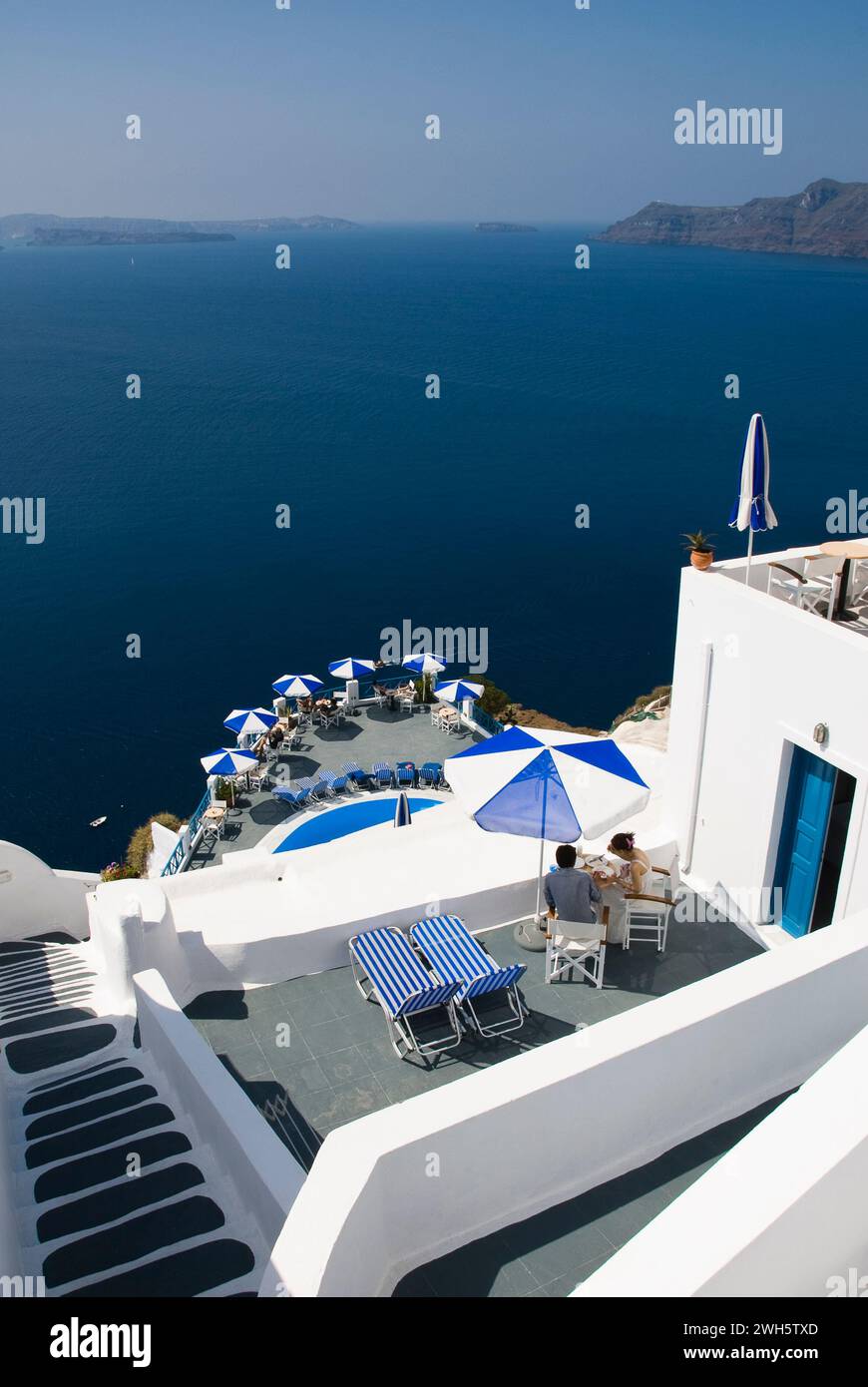 Eine Terrasse mit Stühlen und Sonnenschirmen mit Blick auf das Wasser in Santorin, Griechenland. Stockfoto