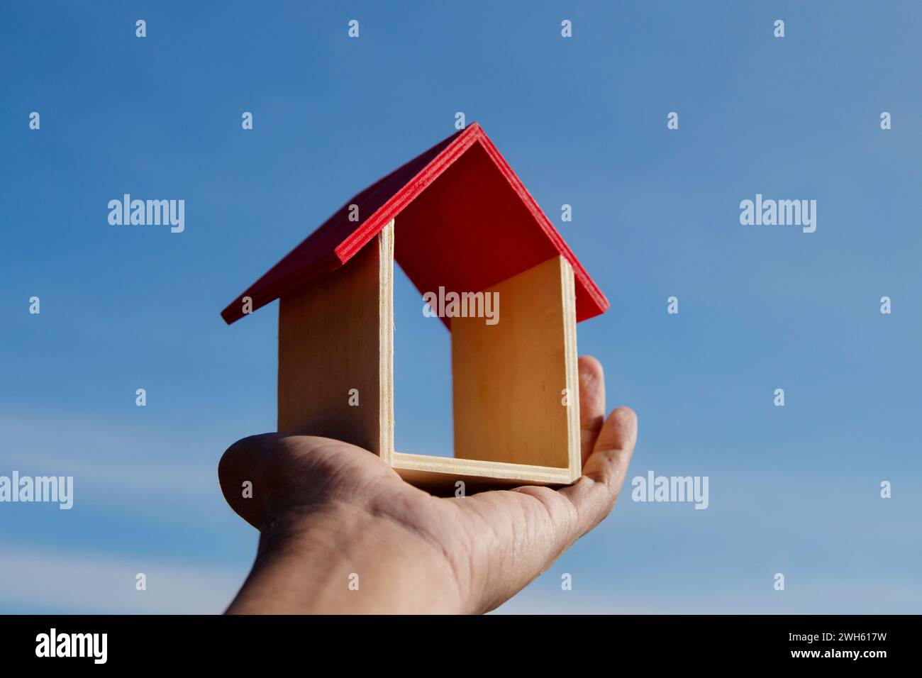 Hand hält Spielzeug Holzhaus mit Hintergrund des blauen Himmels. Traumhaus, Hausbesitz-Konzept. Stockfoto