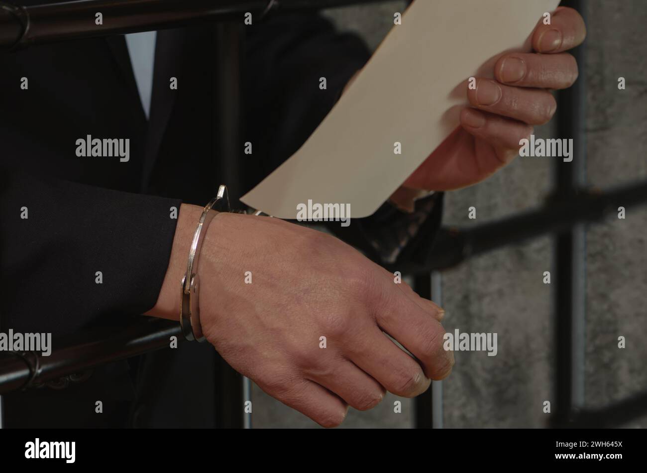 Ein Mann in einem Anzug mit Handschellen am Handgelenk, der ein Stück Papier hält, Zellstangen. Stockfoto