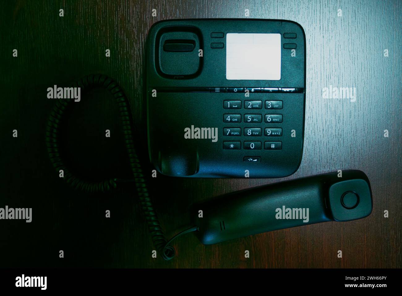 Ein elegantes schwarzes Telefon und das Mobilteil liegen auf einem Schreibtisch und verkörpern moderne Kommunikationstechnologie in einem modernen Büroarbeitsplatz. Stockfoto