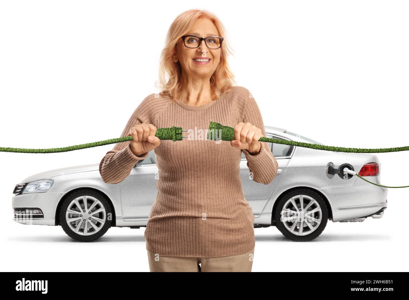 Glückliche reife Frau, die grüne elektrische Kabel für ein Elektroauto auf weißem Hintergrund anschließt Stockfoto