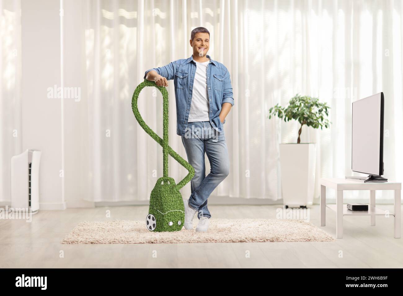 Mann mit einem umweltfreundlichen und effizienten Staubsauger, der zu Hause in einem Wohnzimmer steht Stockfoto