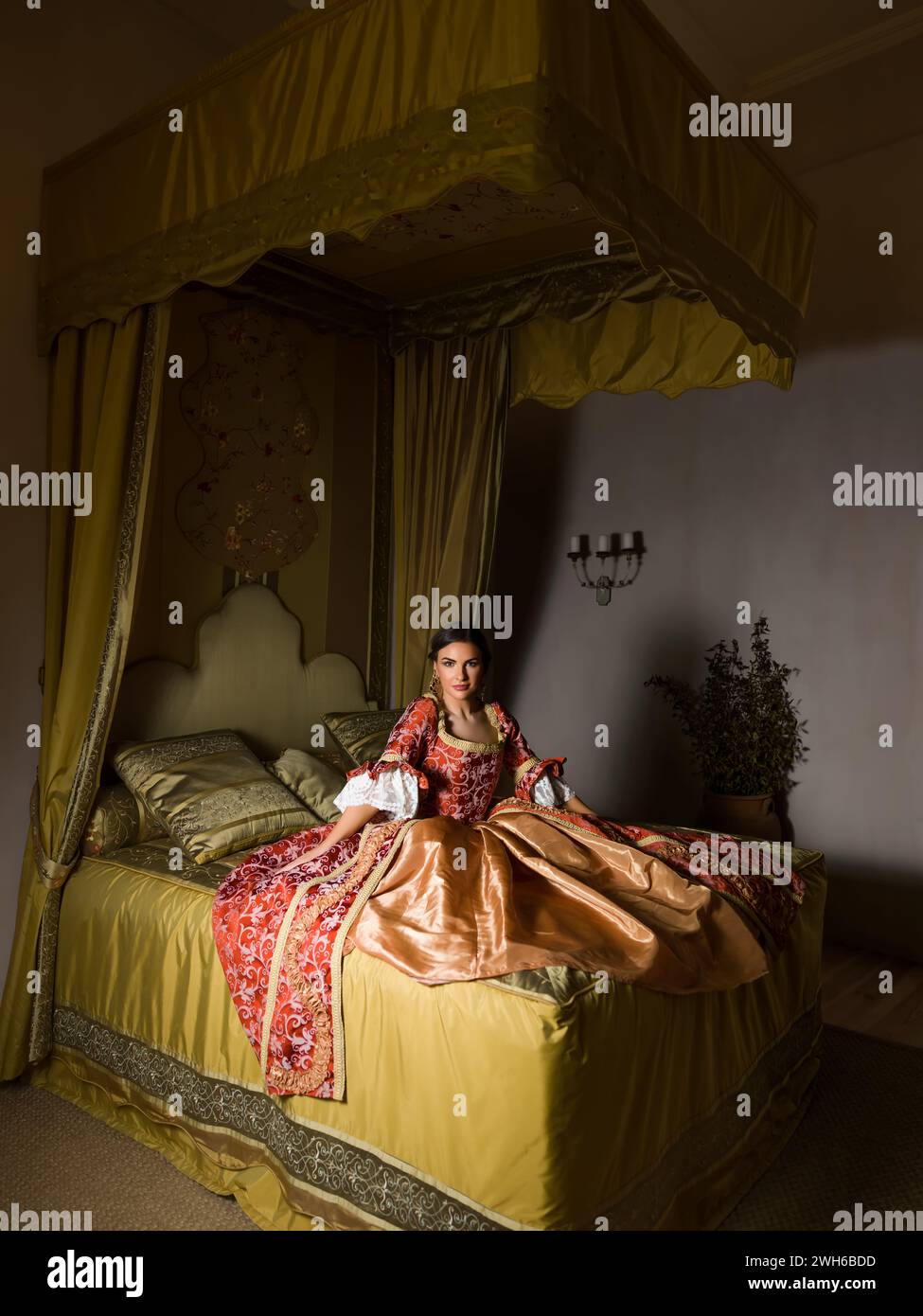 Goldenes mittelalterliches Schlafzimmer mit schönem Himmelbett. Eine Dame im Renaissance-Kleid sitzt auf dem Bett. Stockfoto