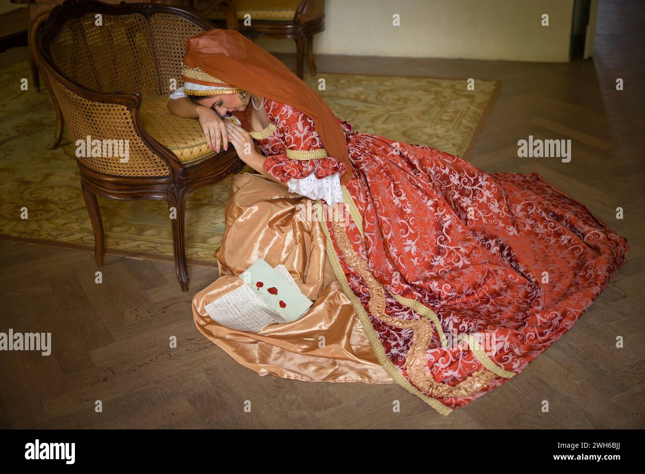 Junge Frau in mittelalterlichem Renaissance-Kostüm und französischer Kapuze, die mit einem Brief auf dem Boden sitzt Stockfoto