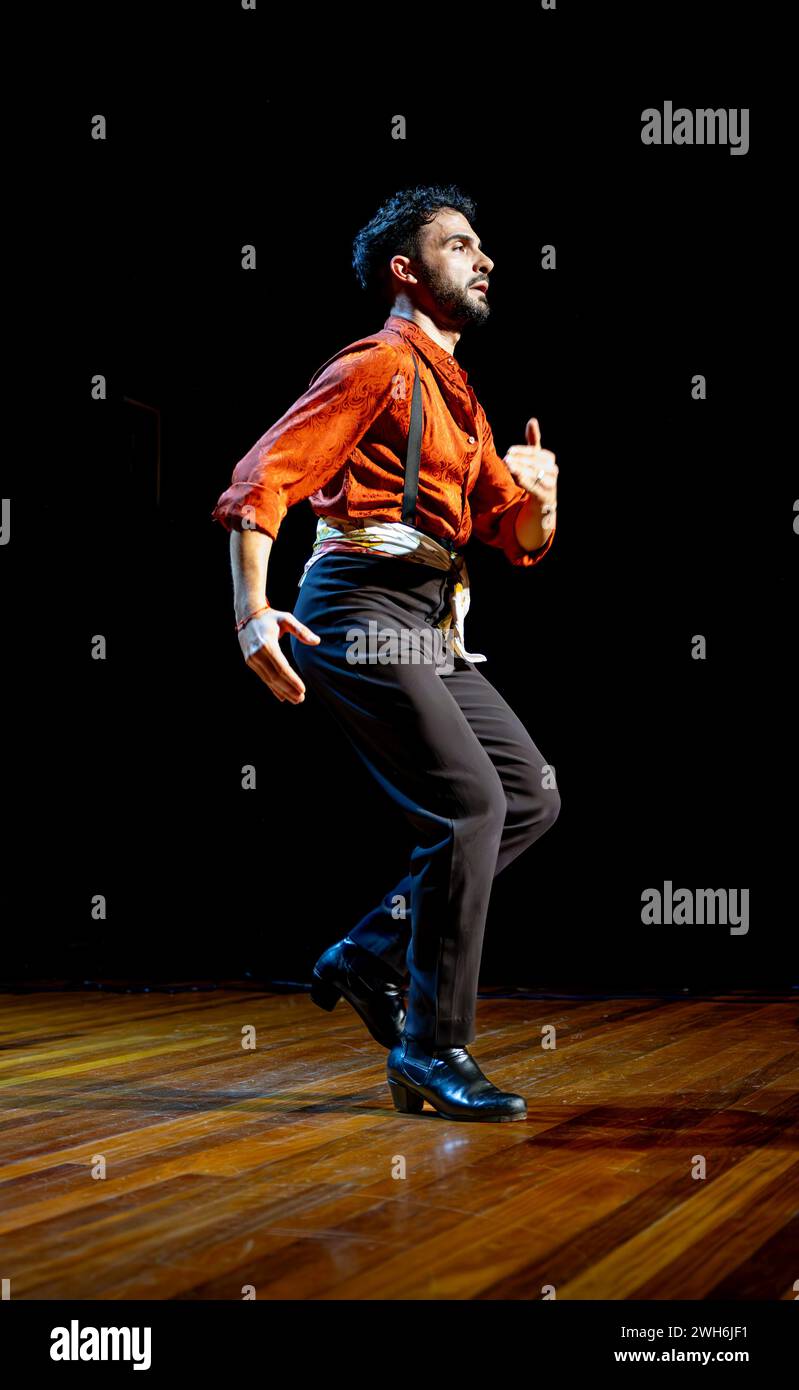 Fokussierter männlicher Flamenco-Tänzer mit traditioneller Kleidung, die auf einer Holzbühne auftritt, verkörpert den Geist des Tanzes, vertikales Foto. Stockfoto