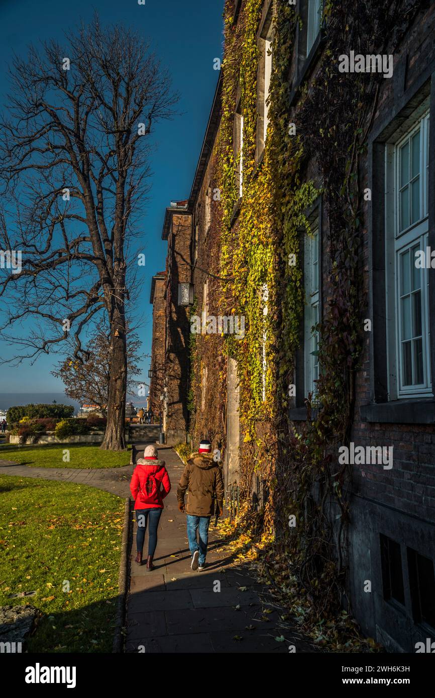 Ein Paar, das an einem schönen Tag an einem sonnigen Gebäude und üppigen Bäumen vorbeischlendert Stockfoto