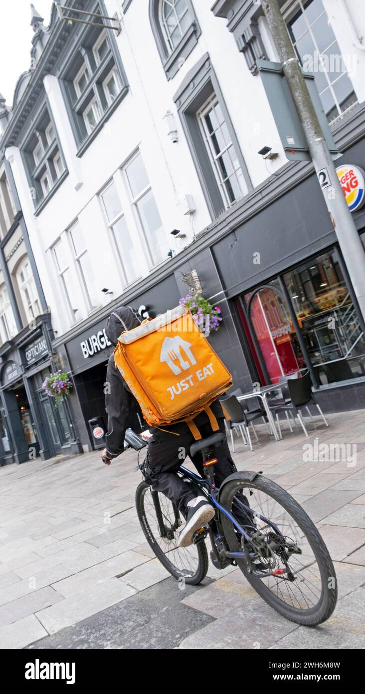 Kurier Radfahrer auf Lieferrad mit Just Eat Rucksack liefert Essen Radfahren auf der Straße in Cardiff City Centre Wales UK KATHY DEWITT Stockfoto