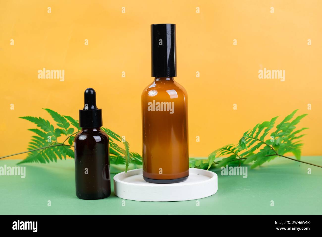 Glasflaschen mit Toner und Serum mit Blättern auf gelbem Hintergrund. Verpackung von Kosmetikprodukten Stockfoto