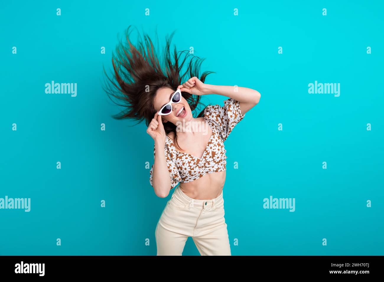 Foto von Freundin junge Fashionista, die ihre gucci Sonnenbrille berührt, Kopf schüttelt fliegende Haare und Tanz isoliert auf cyanfarbenem Hintergrund Stockfoto