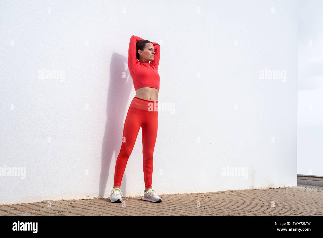 Sportliche Frau, die eine Arm-Dehnübung macht, draußen, weiße Wand. Stockfoto