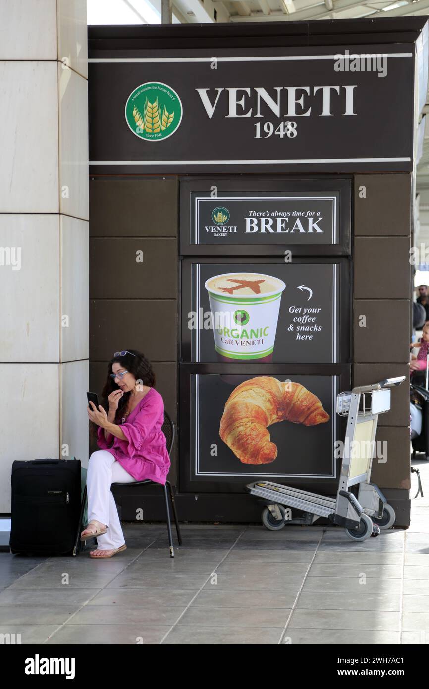 Athen Griechenland internationaler Flughafen Athen (AIA) Eleftherios Venizelos Frau mit Koffer, die auf das Mobiltelefon vor der Bäckerei Veneti blickt Stockfoto