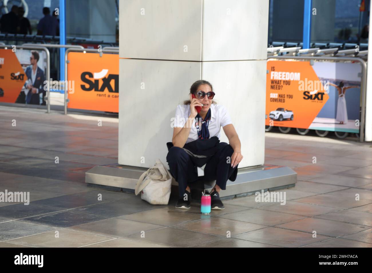 Athen Griechenland internationaler Flughafen Athen (AIA) Eleftherios Venizelos Frau hockt sich vor Terminal zwei beim Sprechen auf dem Mobiltelefon Stockfoto