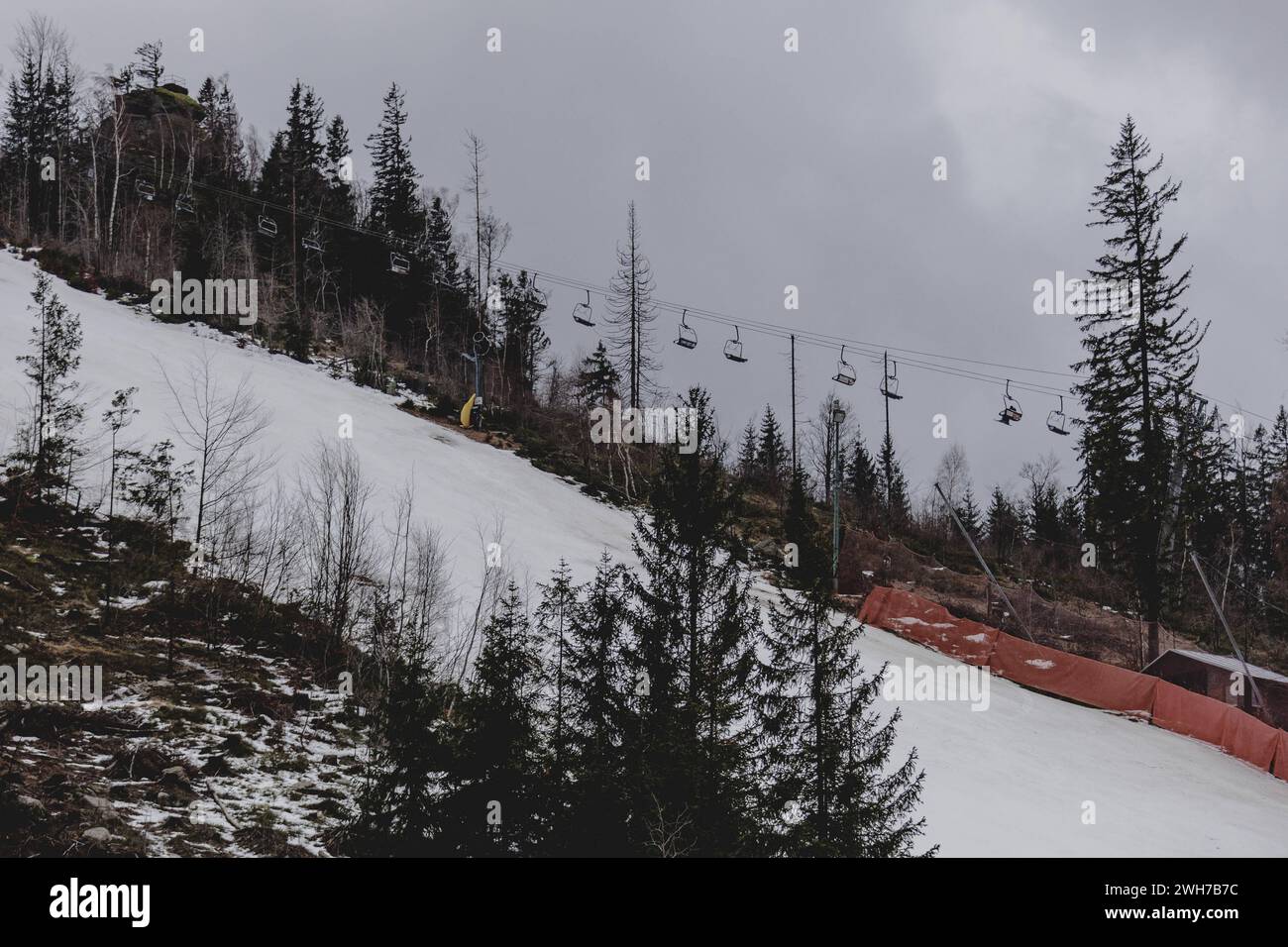 Ein Sessellift zeichnet sich ab zwischen einzelnen Baeumen einer ausgeduennten Waldflaeche, aufgenommen auf einer Skipiste im Skigebiet Isergebirge be Stockfoto