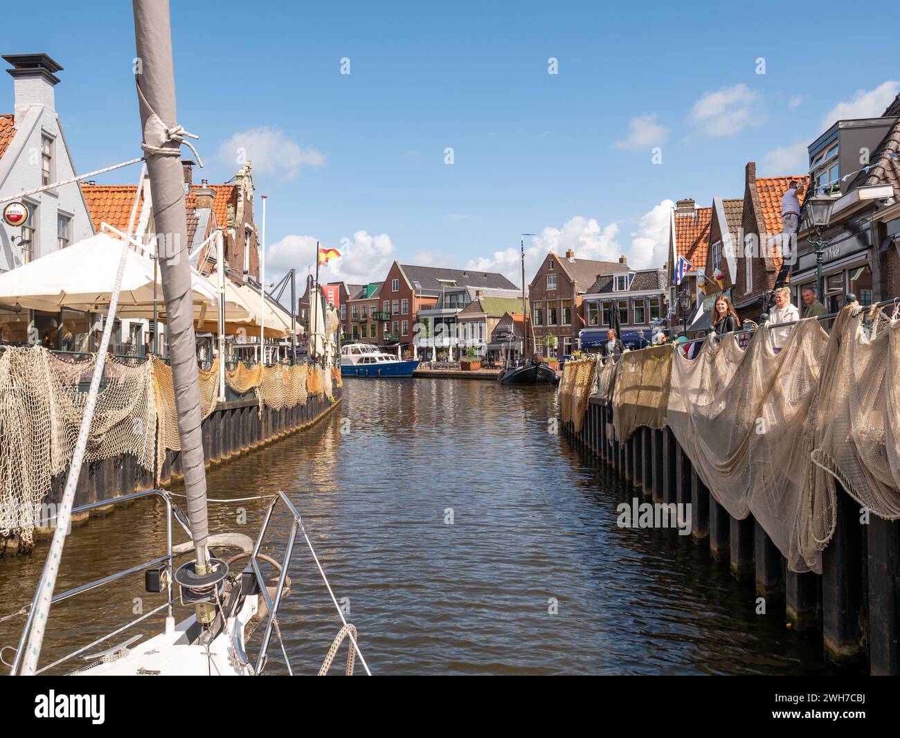 Menschen am Kai Oudesluis beobachten Segelboot im Het Dok Kanal in der Altstadt von Lemmer, Friesland, Niederlande Stockfoto