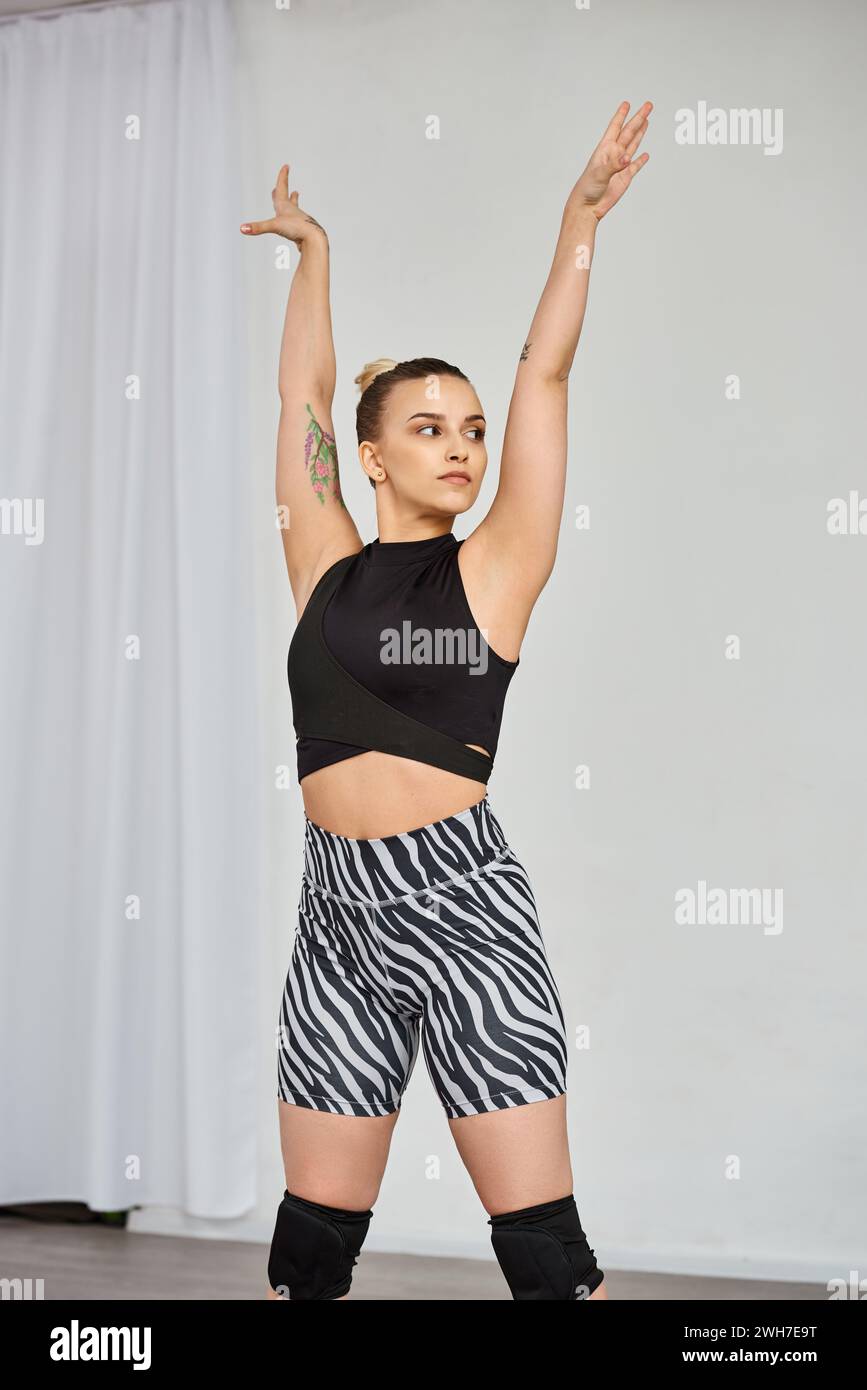 Eine anmutige Frau in einem auffälligen Outfit führt eine dynamische Choreografie durch, während sie ihre Hände hebt Stockfoto