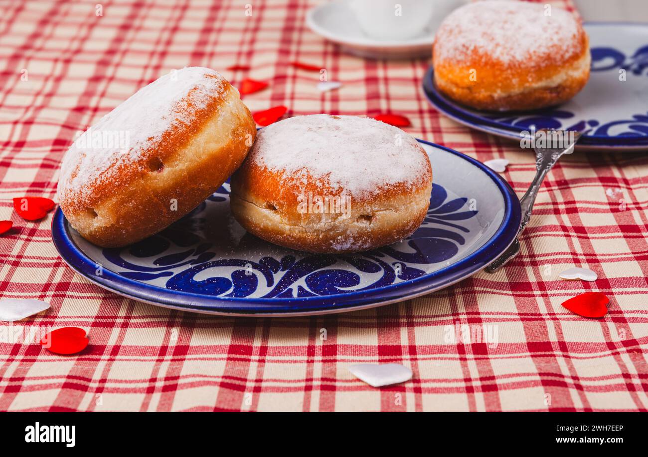 Das Bild zeigt zwei stimulierende Donuts auf einem Teller. Die Donuts sind mit einer Schicht Puderzucker bedeckt und haben eine runde, pralle Form. Stockfoto