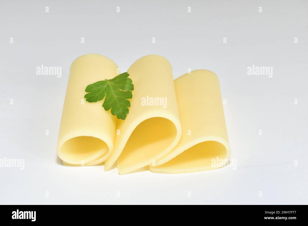 Drei in Röhrchen gerollte Scheiben Gelbkäse liegen auf weißem Hintergrund. Stockfoto