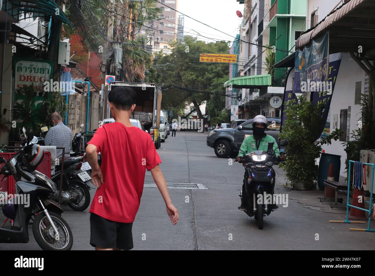 Junge im roten Hemd posiert auf den Straßen, während das Motorrad in Ratchathewi, Bangkok, vorbeifährt Stockfoto