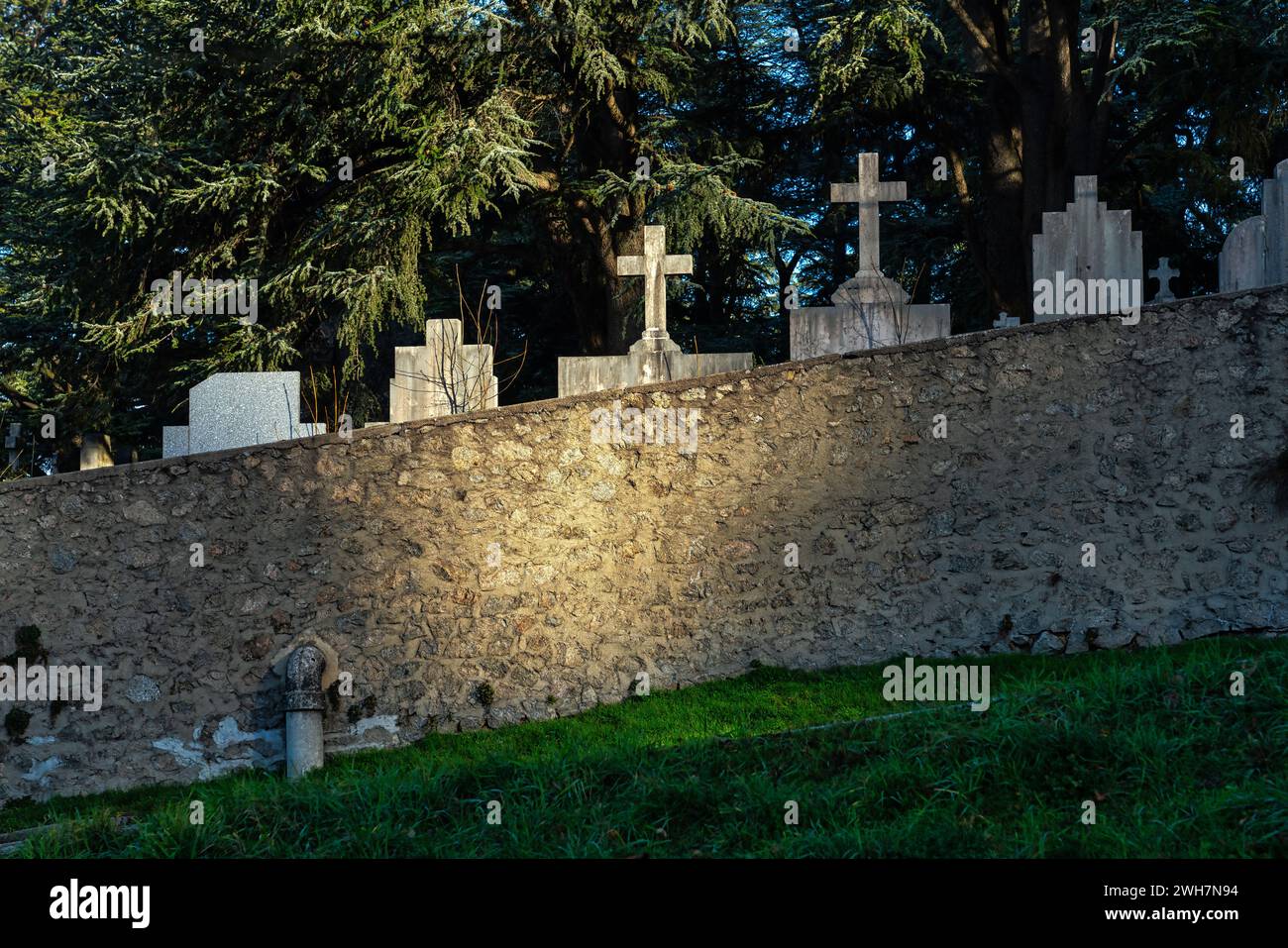Der Friedhof Firminy, die Grabsteine und Kreuze der Gräber, die von einem Sonnenstrahl beleuchtet werden, tauchen aus der umliegenden Mauer auf. Firminy, Frankreich Stockfoto