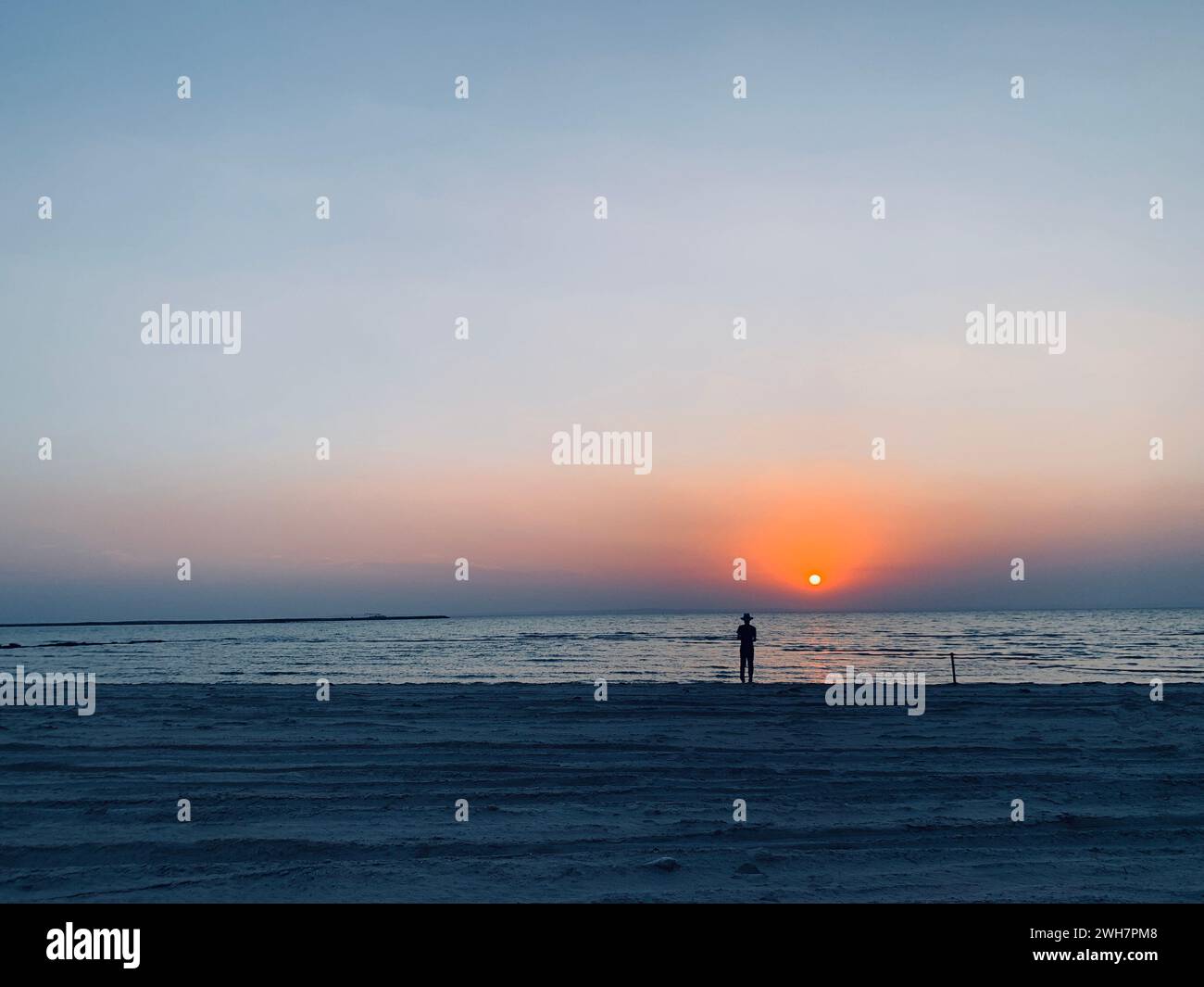 Eine Person, die am Strand steht und bei Sonnenuntergang auf das Meer blickt Stockfoto