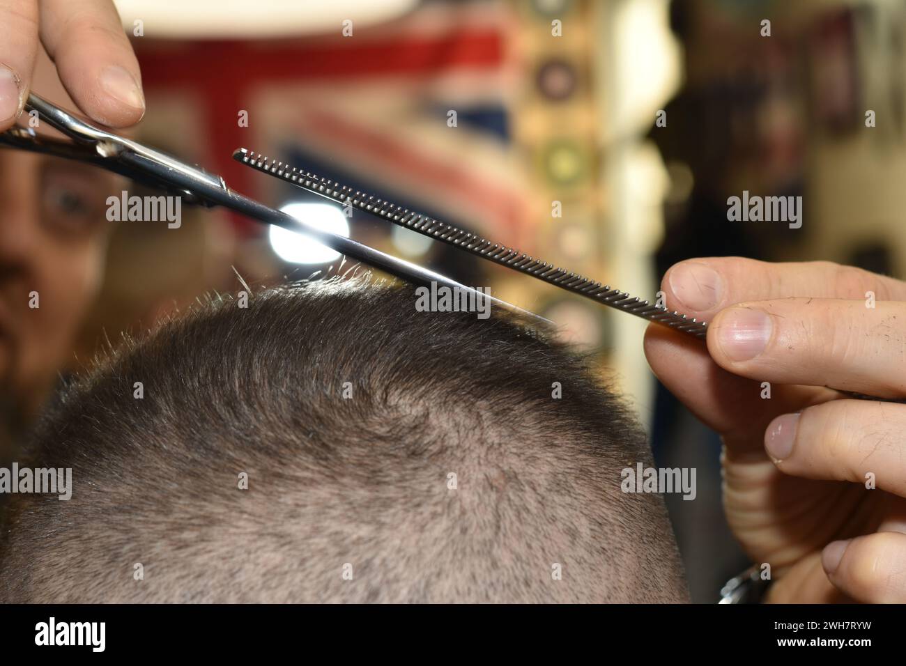 Mit einer Schere und einem Kamm entfernt der Friseur Haare vom Hinterkopf des Kunden. Stockfoto