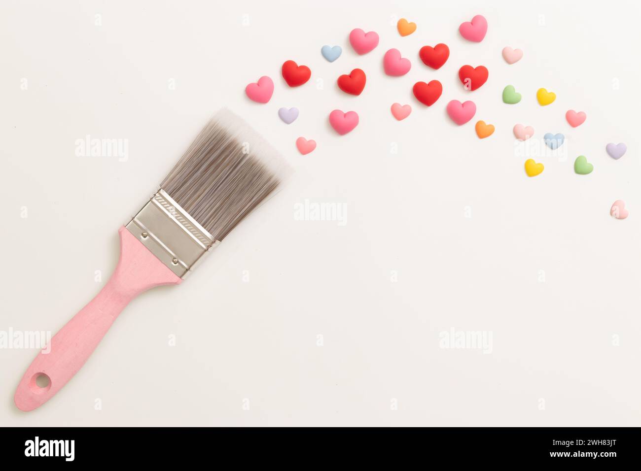 Pinsel mit rosafarbenem Holzgriff, Gemälde mit buntem, winzigem Herz, das auf weißem Hintergrund isoliert ist, dekorieren Sie für Valentinstag-Feier Hintergrund Stockfoto