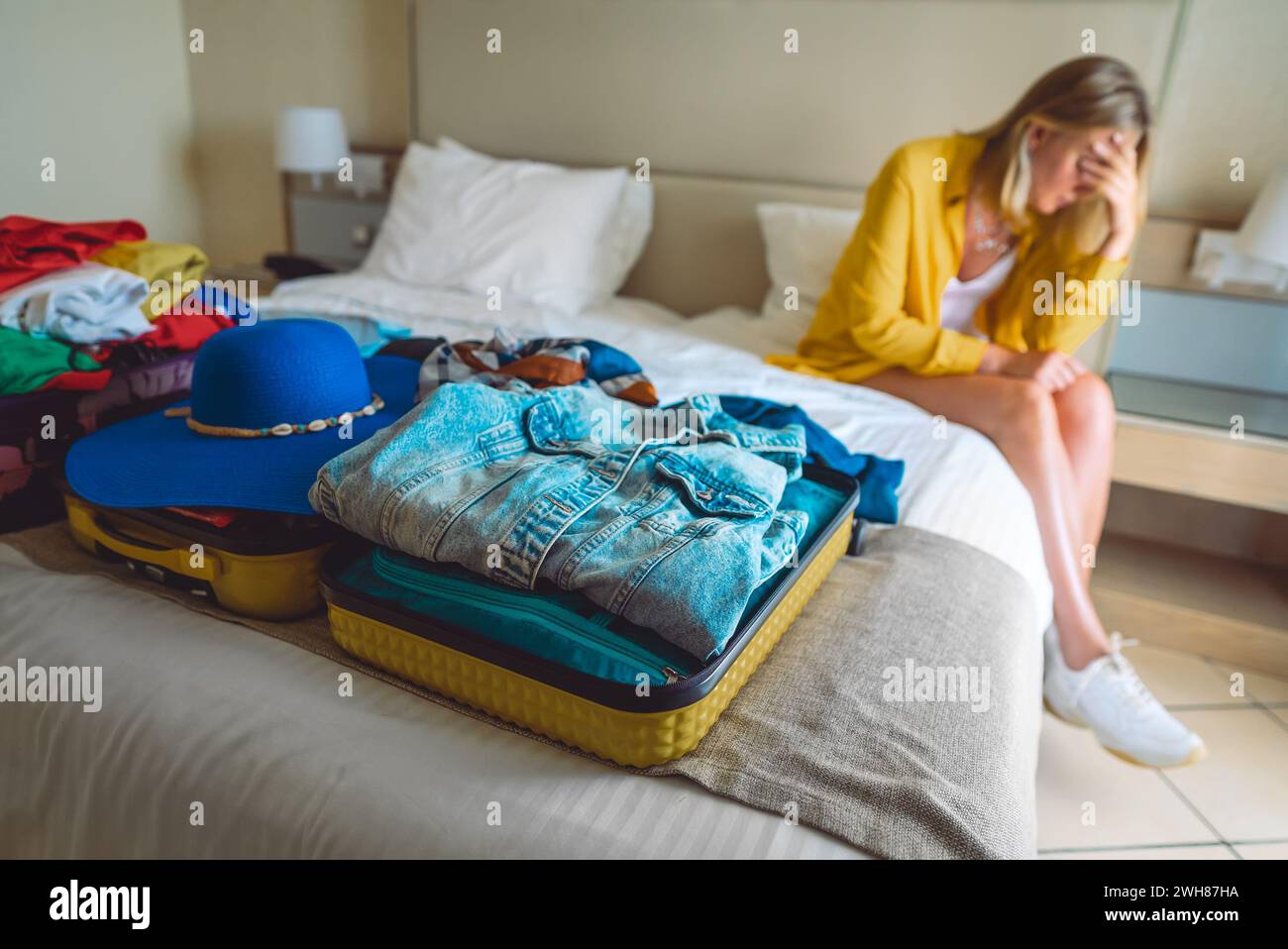 Flugstornierung. Verärgerte Frau, die mit Koffern mit Kleidung auf dem Bett sitzt. Stockfoto