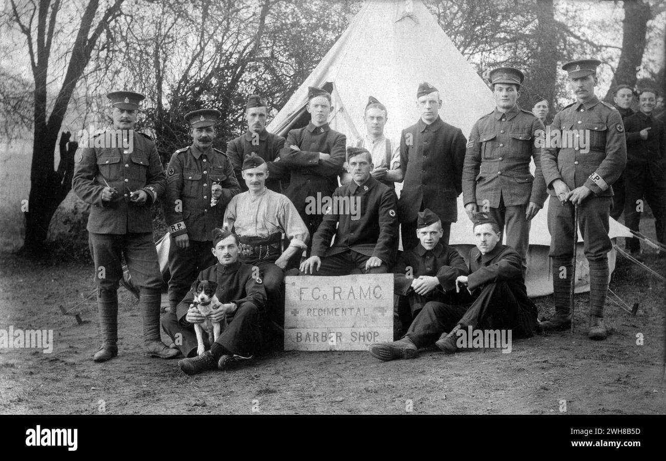 Aldershot, Hampshire. 1914: Britische Soldaten des Regimental Barber Shop (F) Company, Royal Army Medical Corps im Redan Hill Fort, Aldershot, 1914. Die Männer posieren mit ihrem Hundemaskottchen vor einem Glockenzelt. Einige der Soldaten tragen Standard-Khaki mit Regimentsarmbändern. Die übrigen tragen temporäre blaue serge-Uniformen, die als „Kitchener Blues“ bekannt sind. Da das Kriegsministerium in den Anfangswochen des Ersten Weltkriegs keine ausreichende Menge an Standard-Khaki-Uniformen erhalten konnte, wurde diese Alternative als Notmaßnahme eingeführt. Stockfoto