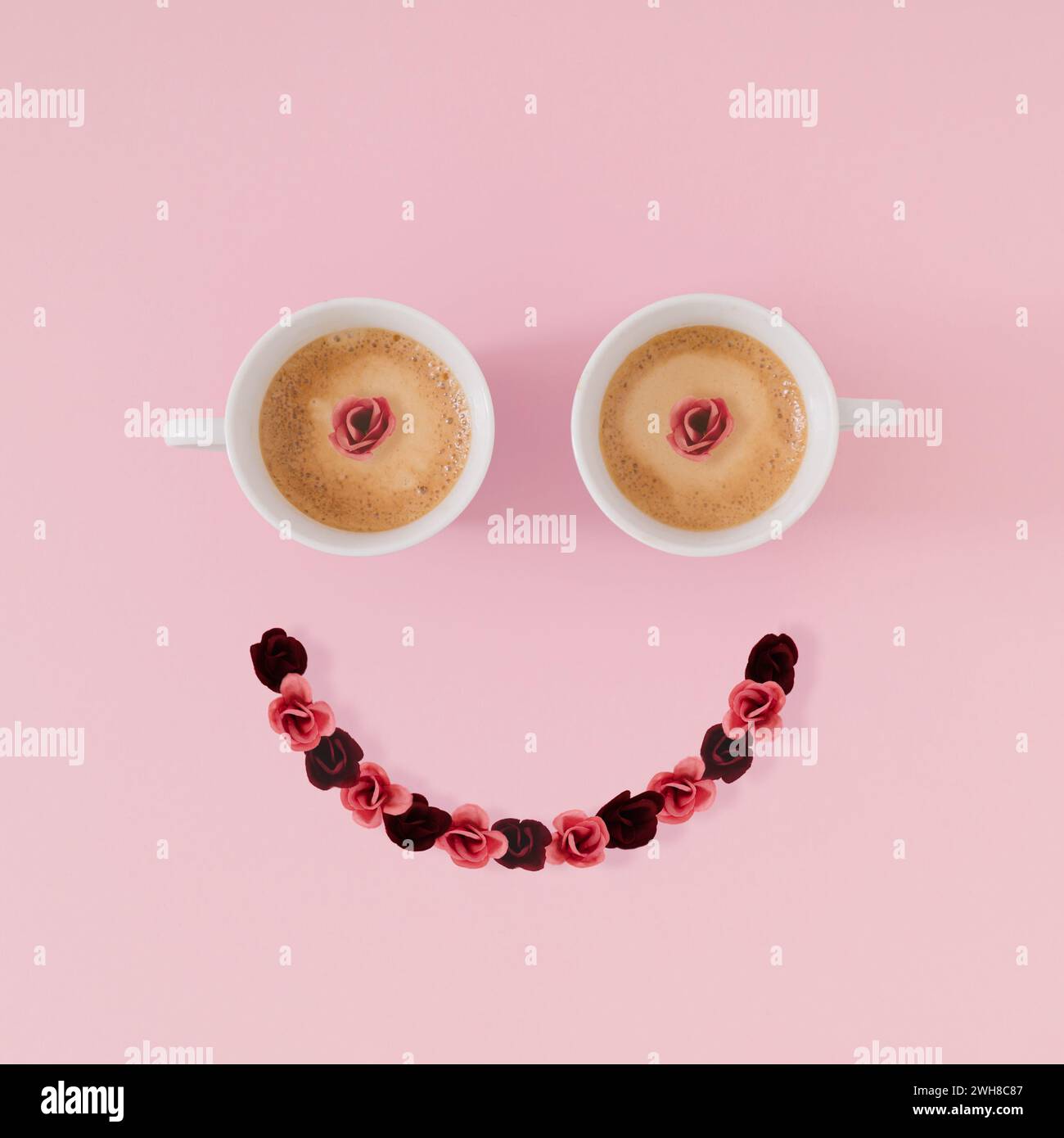 Layout des Smiley Emoticon gemacht mit Kaffeetassen und Blumen auf rosa Hintergrund. Minimales Kaffeekonzept. Kreatives positives Denken und gute Laune-Idee. Stockfoto