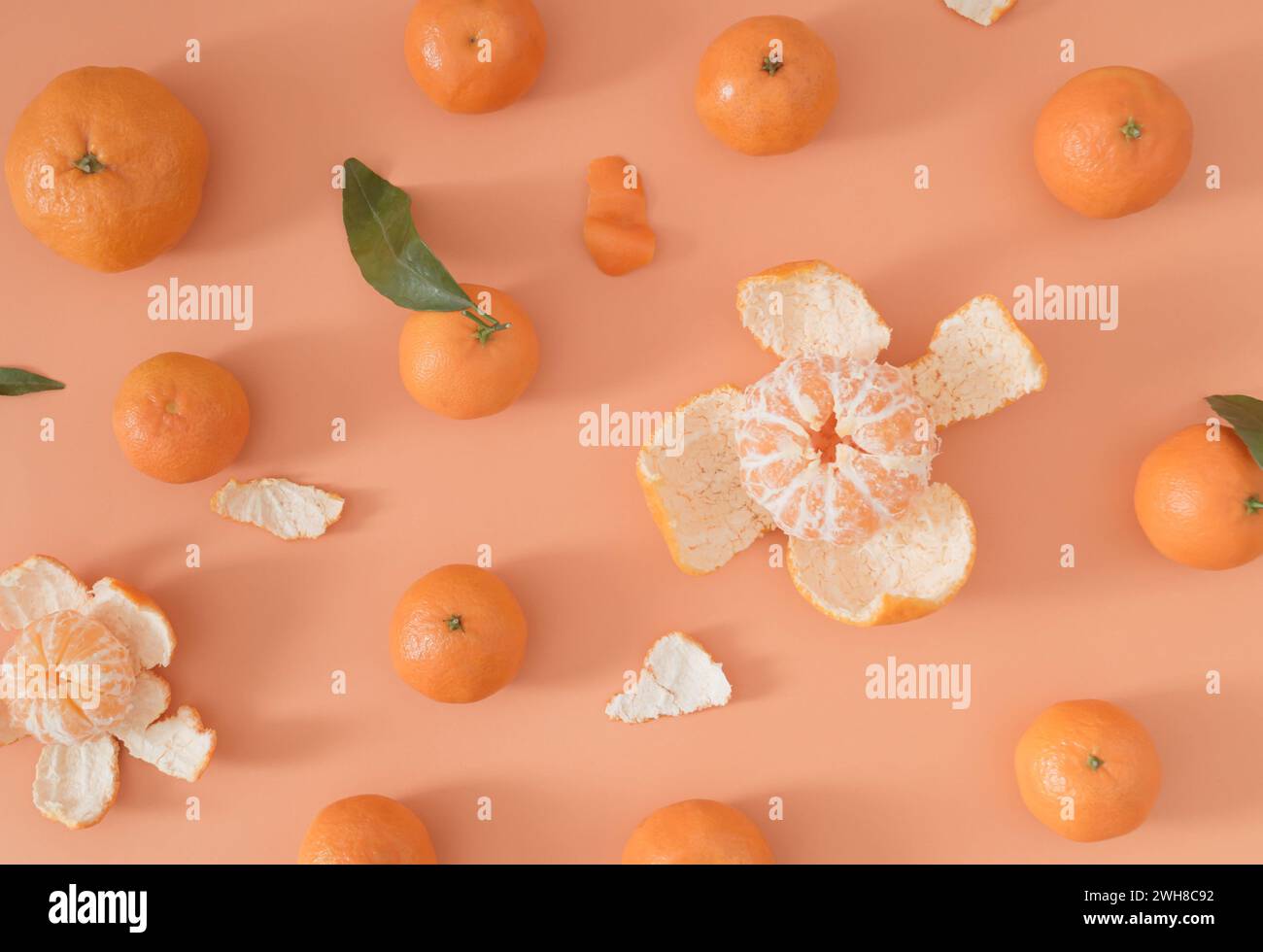Trendiges Fruchtmuster aus vielen frischen Reifen Mandarinen und grünen Blättern auf hellem pfirsichfarbenen orangen Hintergrund. Minimales Zitrusfrucht-Konzept. Stockfoto