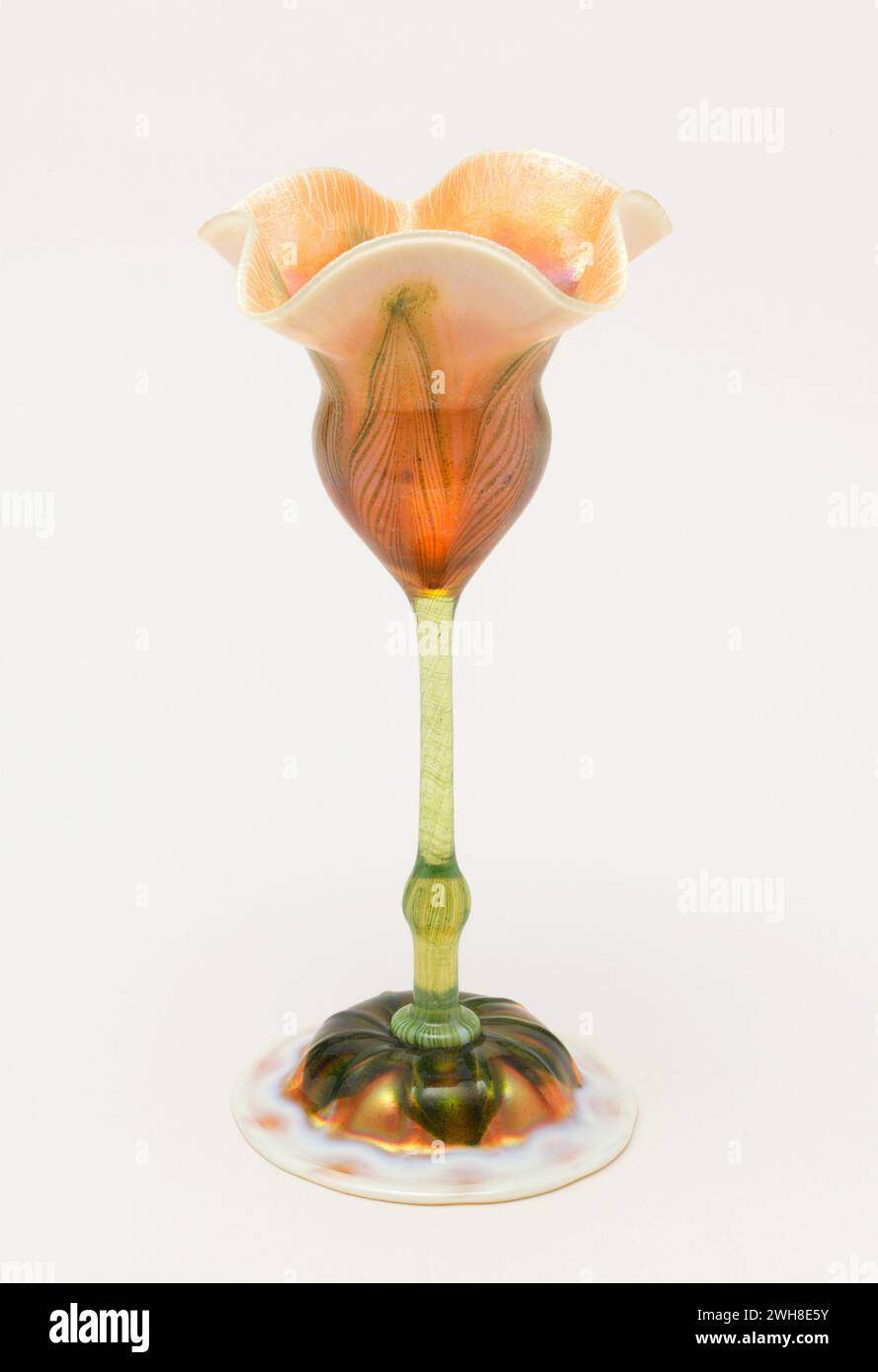 Louis Comfort Tiffany Blumenförmige Vase. Flache runde Basis, schmaler, geknöpfter Stiel und abfackelnde „Tulpe“ – Oberseite aus Opal- und Bernsteinglas, mit grünen Sprenkeln und Streifen an Basis und Stiel, die oben blumenförmige Adern bilden. Stockfoto