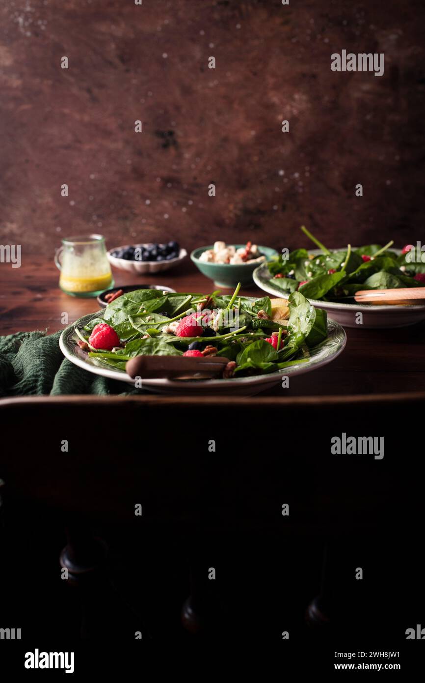 Ein gesunder grüner Salat mit Spinat und Apfel und Himbeeren in zwei Schüsseln auf einem Holztisch Stockfoto