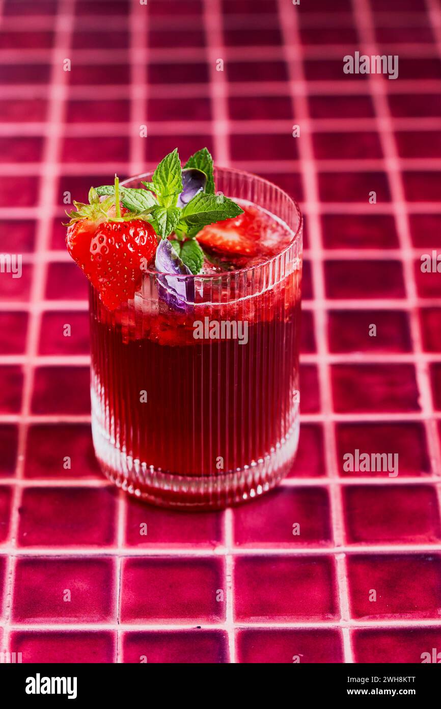Erdbeer-Hibiskus-Minde-Basilikum-Spritz-Tee auf rotem Fliesenhintergrund mit Garnish Stockfoto