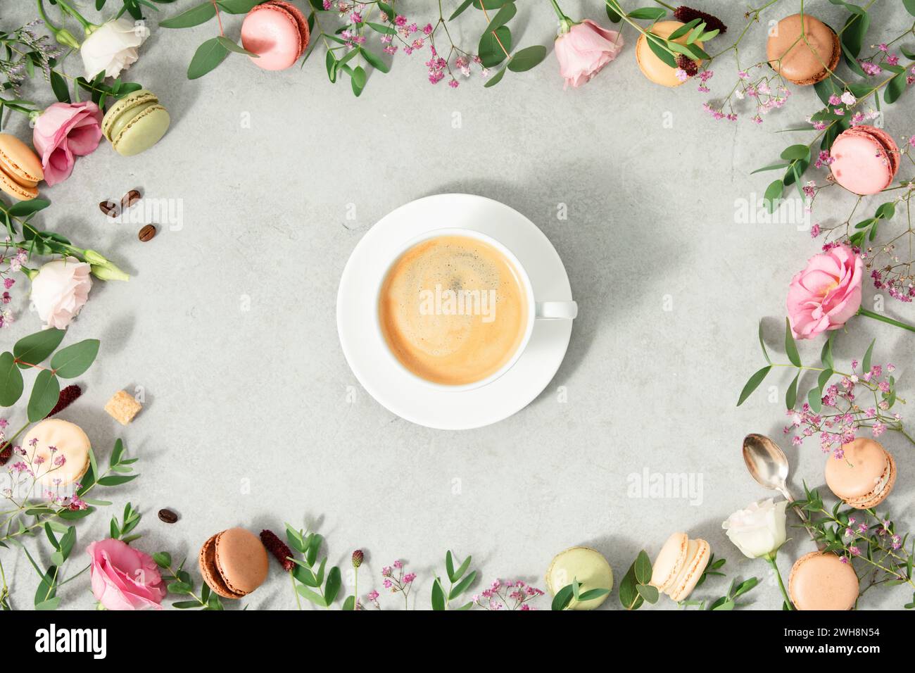 Weiße Tasse Kaffee und Rahmen aus Frühlingsblumen und verschiedenen Arten von Makronen flach gelegt Stockfoto