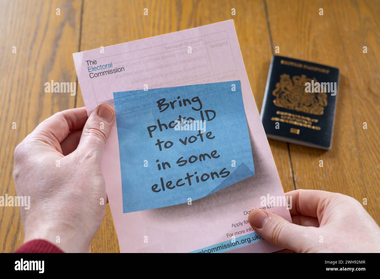 Ein Mann mit einem Flyer der wahlkommission, in dem angegeben wird, dass bei einigen Wahlen ein Lichtbildausweis erforderlich ist, mit einem britischen Reisepass im Hintergrund. England Stockfoto
