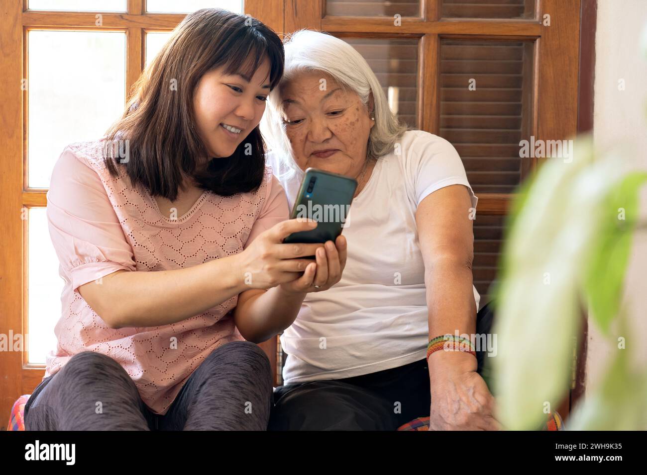 Japanische Erwachsene Tochter teilt Fotos, die mit ihrem Smartphone aufgenommen wurden, mit ihrer älteren Mutter. Stockfoto