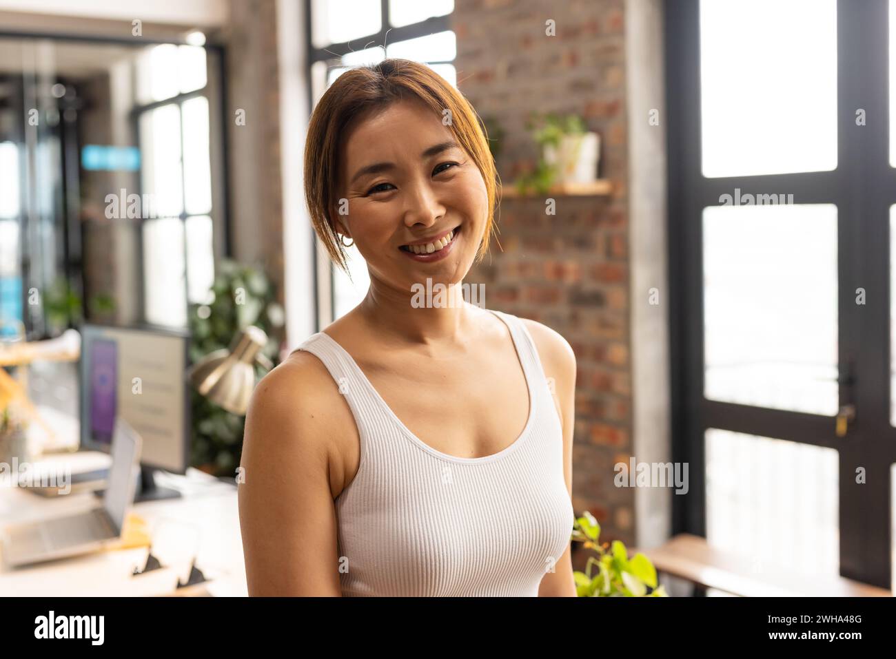 Asiatische Frau lächelt hell in einem sonnigen, zwanglosen Geschäftsbüro Stockfoto