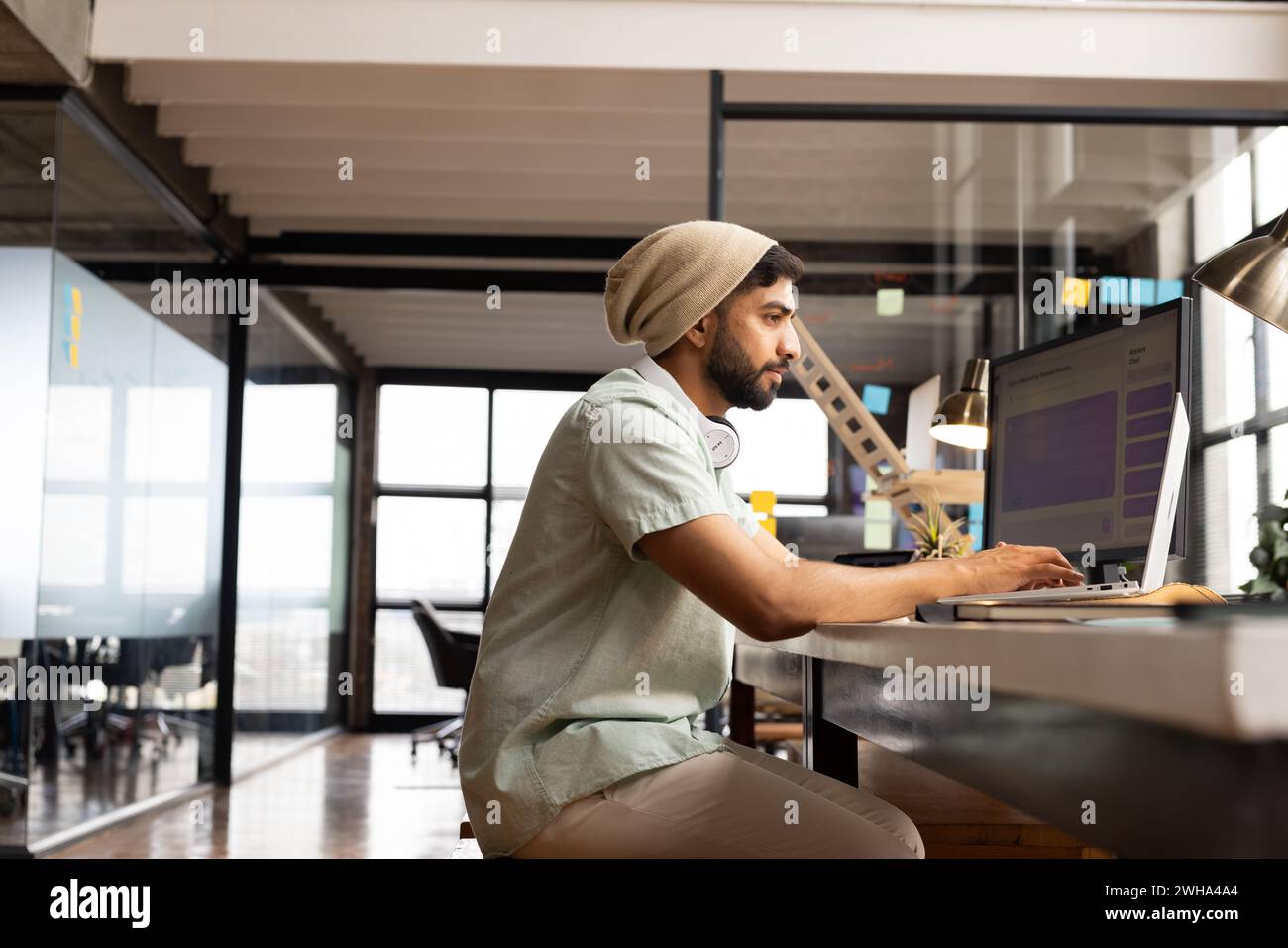 Ein junger asiatischer Mann arbeitet intensiv an seinem Computer in einem zwanglosen Geschäftsbüro Stockfoto