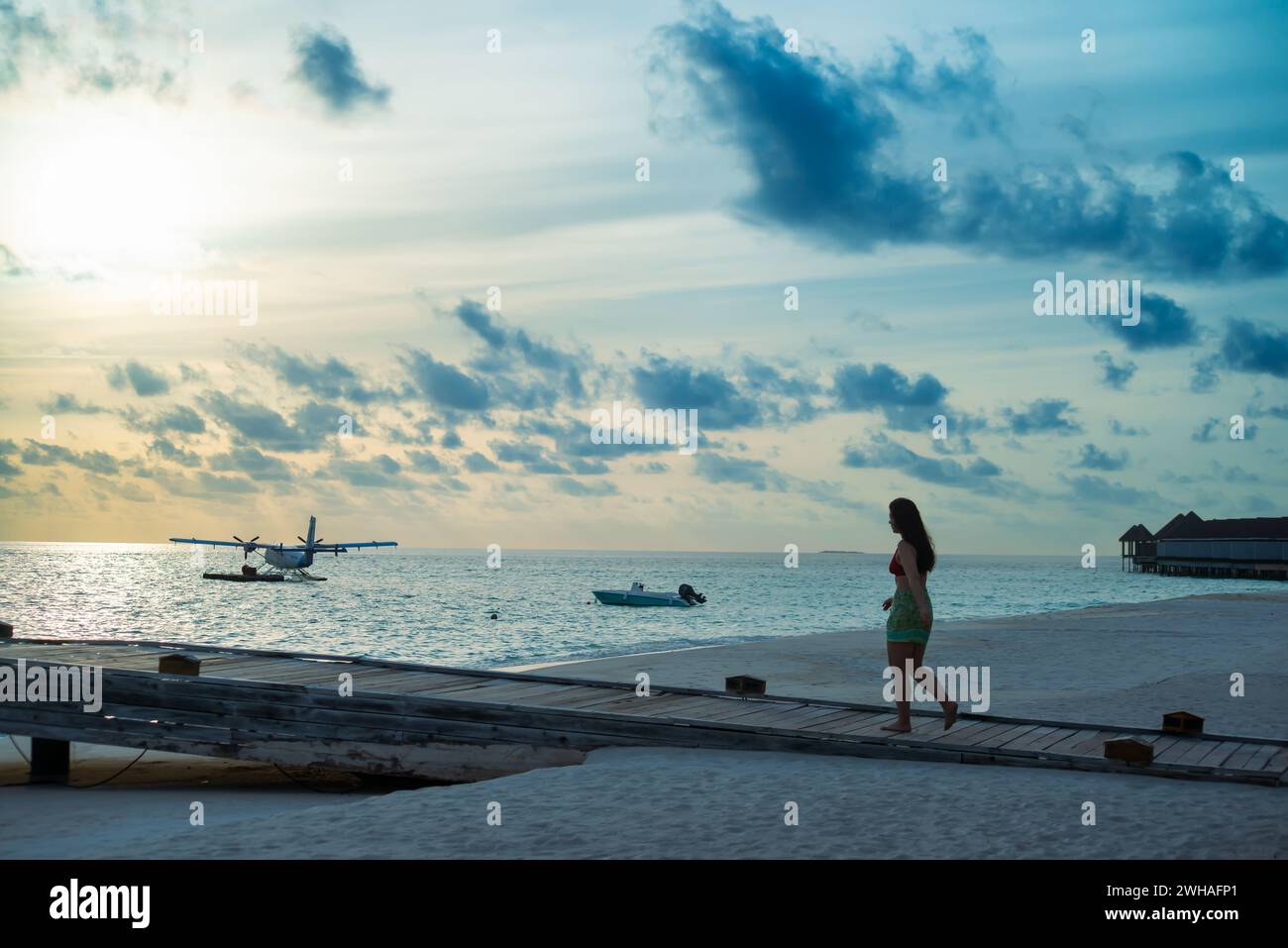 Ein malerischer Blick auf ein Meeresflugzeug am maledivischen Meer, mit einer Frau, die auf dem Dock spaziert, schafft einen idyllischen und ruhigen Küstenort im Paradies Stockfoto