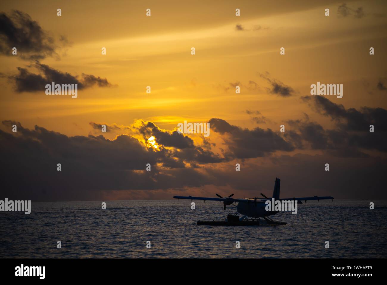 Ein faszinierender Sonnenuntergang über den blauen Malediven, mit einem Wasserflugzeug, das über das türkisfarbene Meer gleitet, schafft eine idyllische und ruhige Insel Stockfoto