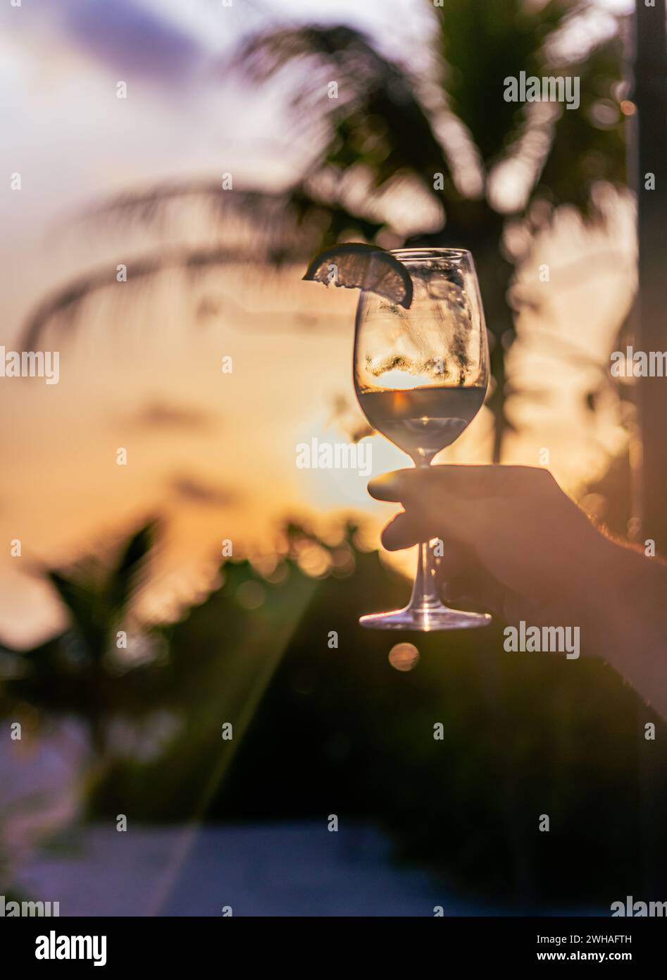 Ein fesselnder Moment mit einem Cocktailglas beim maledivischen Sonnenuntergang, der exotische Aromen mit der ruhigen Schönheit des Küstenparadieses verbindet. Stockfoto