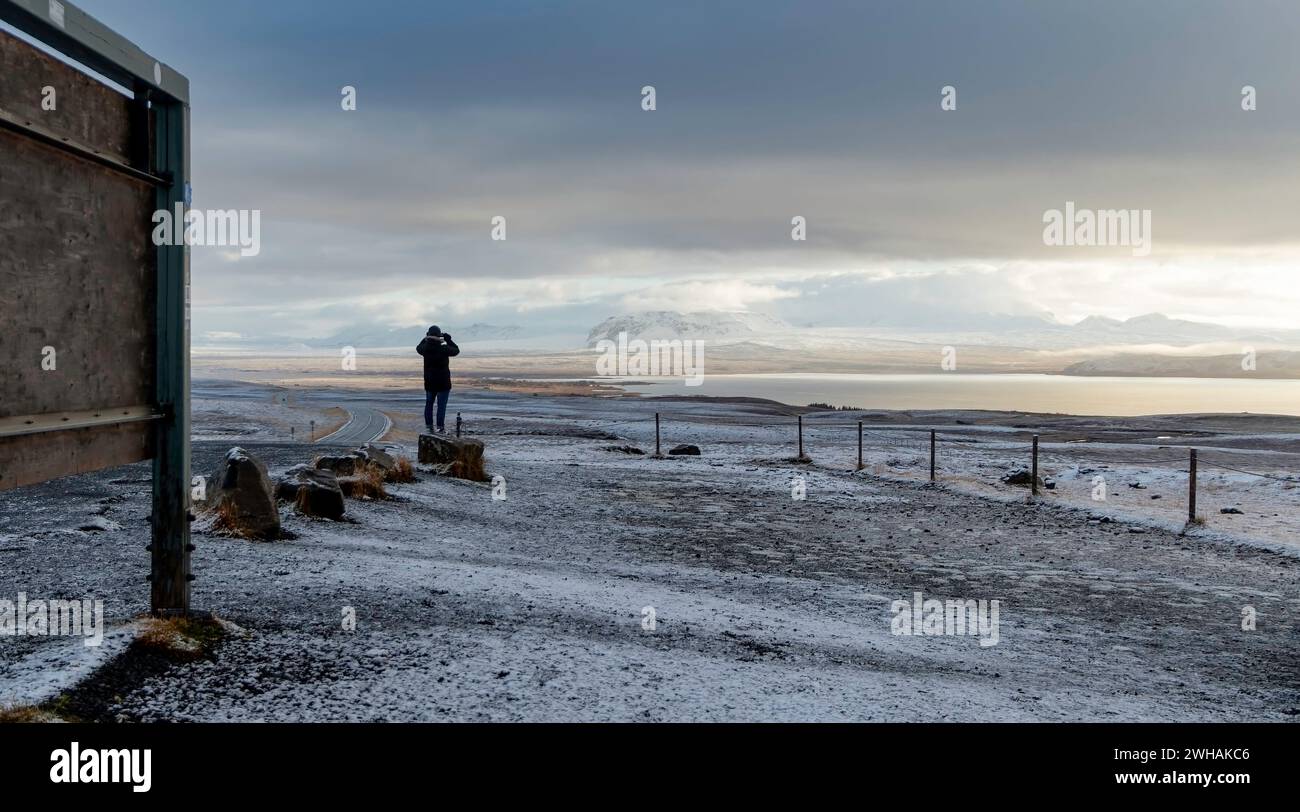 Anonyme Person aus der Ferne stehend und genießt die atemberaubende Landschaft der ruhigen Natur in der Nähe des Seeufers bei Sonnenuntergang vor grauem Himmel Stockfoto