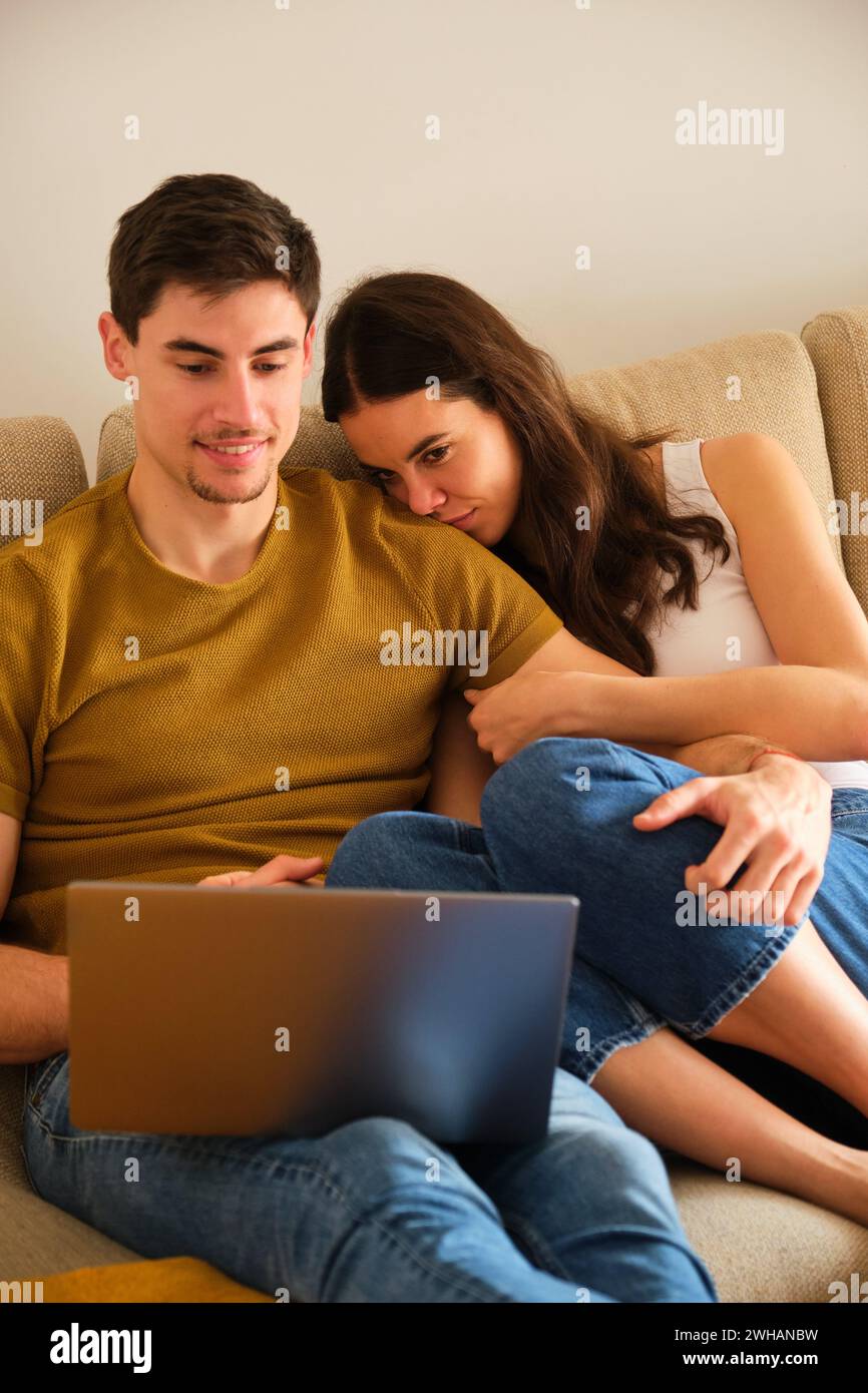 Ein spanisches Paar sieht sich einen Film auf dem Laptop an, während er sich umarmt und küsst. Stockfoto