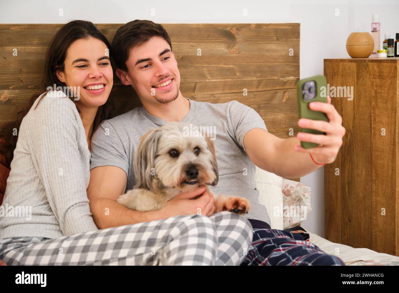 Spanisches glückliches Paar, das ein Selfie mit seinem Hund im Bett macht. Stockfoto