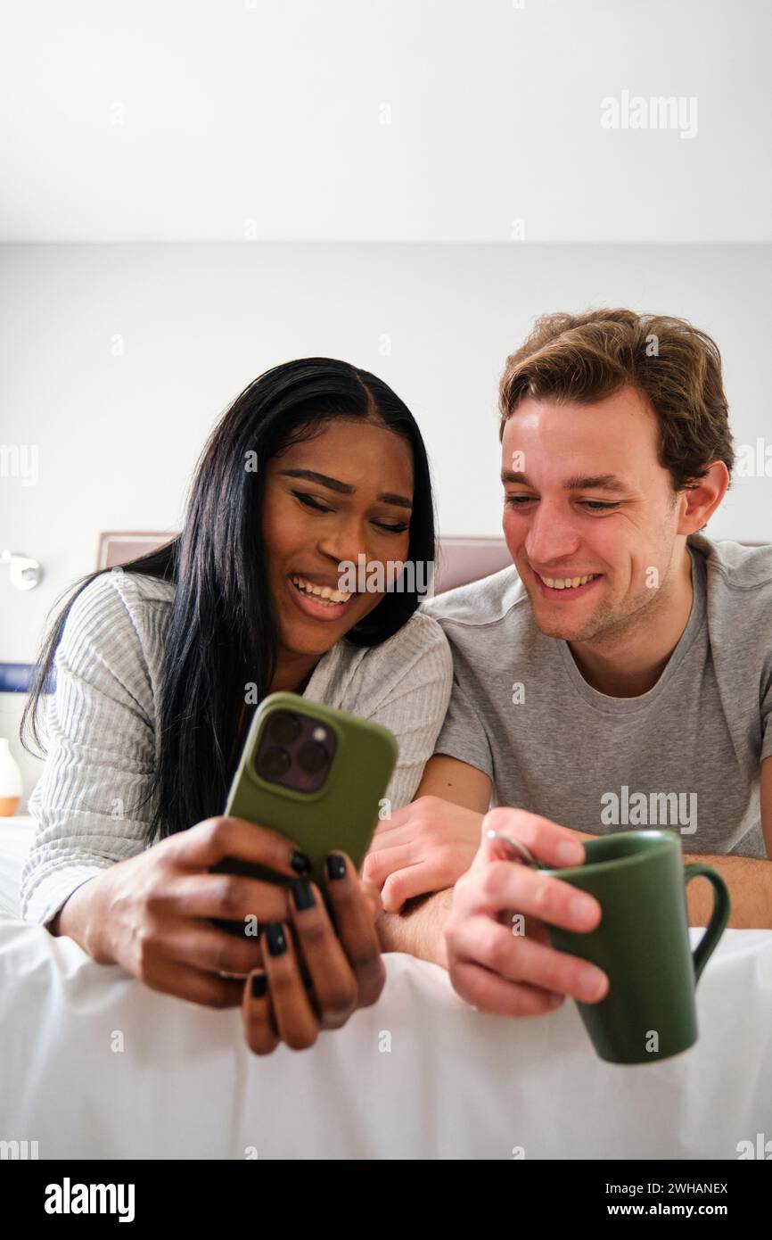 Multiethnische Paare lachen beim Ansehen von Videos auf dem Smartphone. Stockfoto